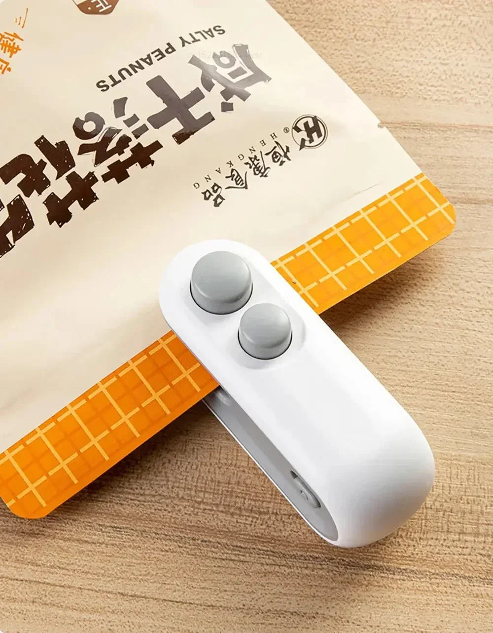 White plastic bag clip sealing a beige and orange packet of salty peanuts on a wooden surface